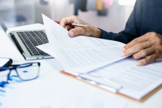 © stock.metket.com - stock.adobe.com Foto: Person mit Dokumenten und Laptop