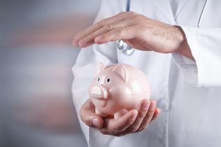 © andranik123 - stock.adobe.com Foto: Arzt hält Hand über Sparschwein